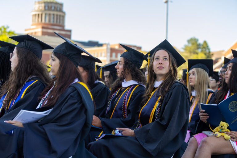 University of Rochester graduates listen during the Commencement Weekend ceremony with Rush Rhees Library in the background.