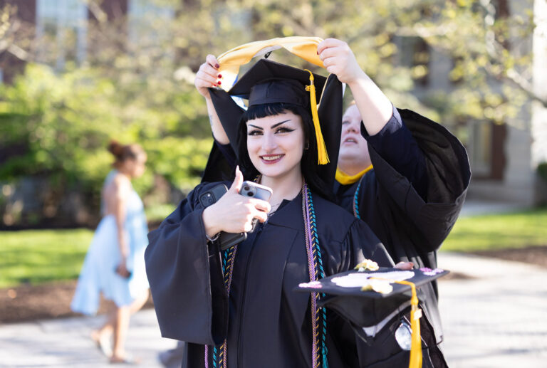 A University of Rochester graduate smiles as another graduate helps place her academic hood during Commencement Weekend.