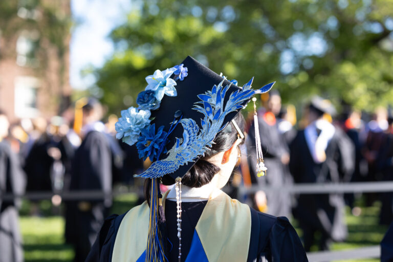 A University of Rochester graduate wears a decorated cap with blue flowers and a bird design during Commencement Weekend.