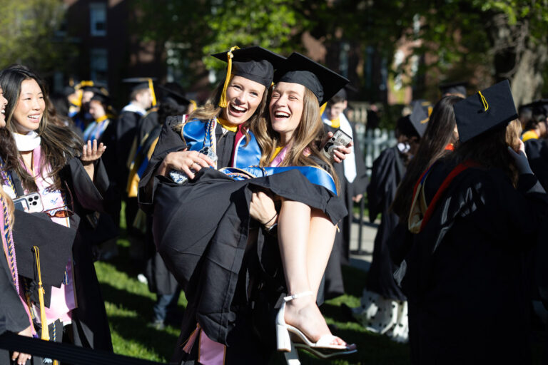 Two University of Rochester graduates laugh as one lifts the other for a photo during Commencement Weekend.