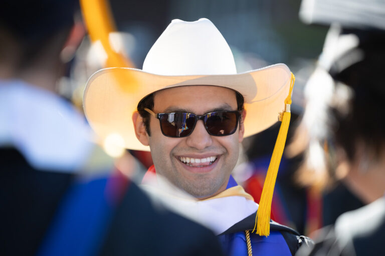 A University of Rochester graduate smiles while wearing a white cowboy hat over his cap during Commencement Weekend.