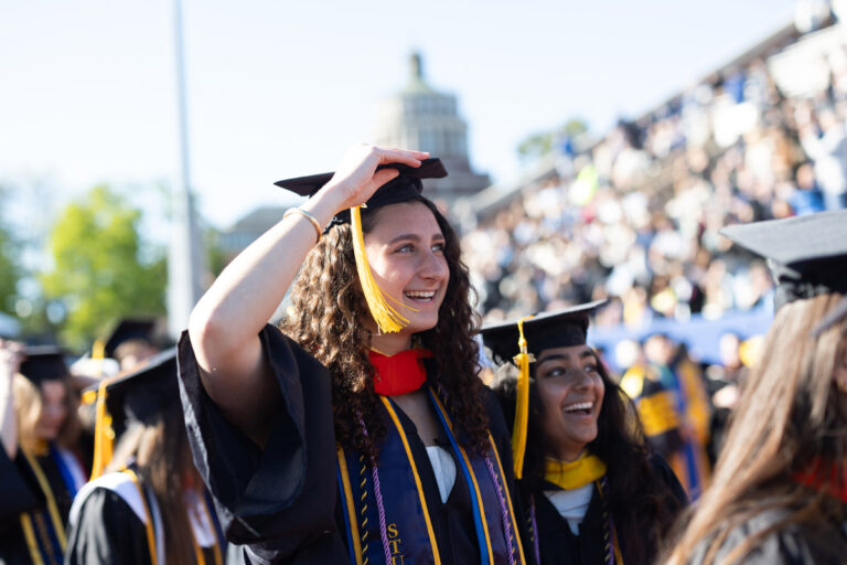 A University of Rochester graduate smiles while adjusting her cap during Commencement Weekend.