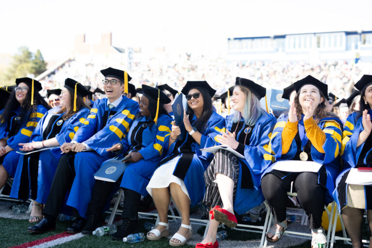 University of Rochester graduates in blue academic regalia smile and applaud during Commencement Weekend.
