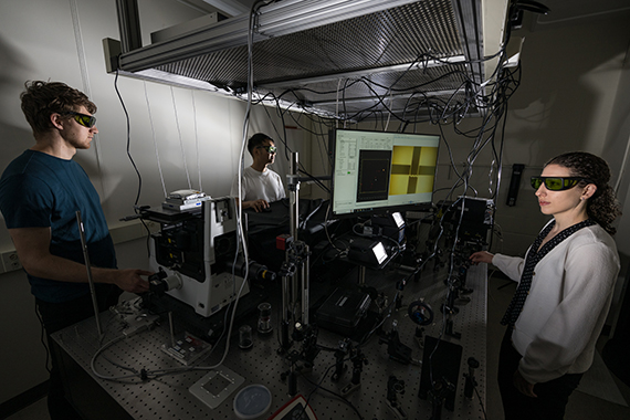Three people wearing protective eye gear in a lab demonstrate heat transfer mapping techniques that are displayed on a computer screen.