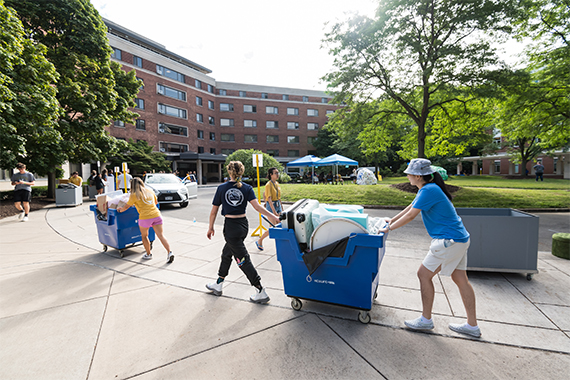 Students push carts full of their belongings in the traffic circle in front of Susan B Anthony Hall.
