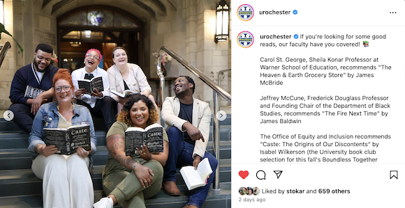 Several University staff members sit on the steps holding copies of "Caste: The Origins of Our Discontents" by Isabel Wilkerson