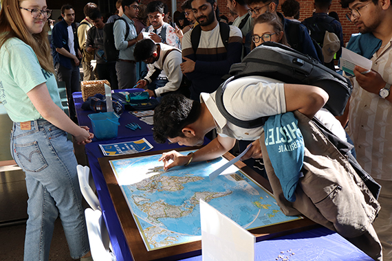 A student places a pin on a world map during a crowded graduate orientation event.