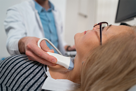 A medical provider holds an ultrasound wand to a patient's neck.