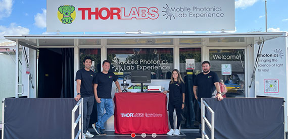 Four employees pose in front of a ThorLabs Mobile Photonics Lab Experience trailer.