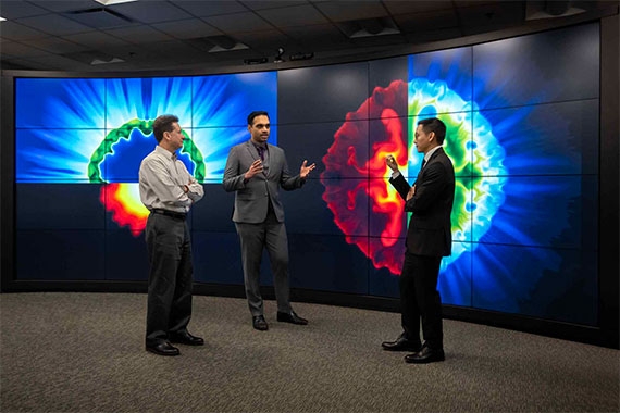 Three men stand in front of a giant screen discussing AI and fusion research visualizations on display.