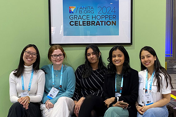 Five data science students sit in front of a poster that says "Anita B.org 2024 Grace Hopper Clebration."