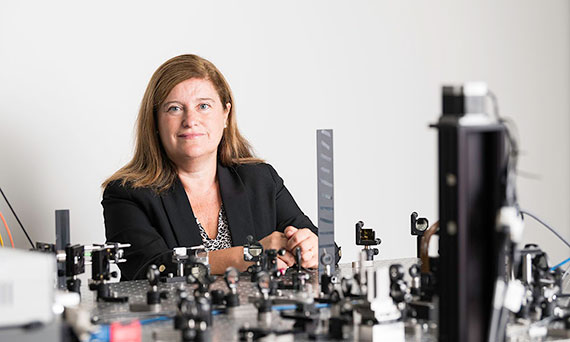 Susana Marcos looks at the camera while posed behind a large optical bench filled with experiments.