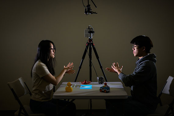 Two people sit across from a table using American Sign Language, artificial intelligence, and augmented reality to test a tabletop system for parents of deaf and hard-of-hearing children.