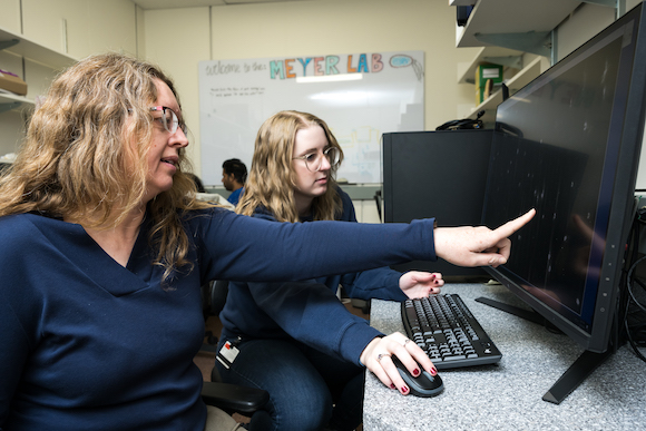 Professor and graduate student in lab, with professor pointing to a computer screen