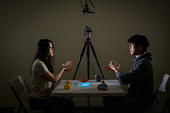 Two people sit across from a table using American Sign Language, artificial intelligence, and augmented reality to test a tabletop system for parents of deaf and hard-of-hearing children.