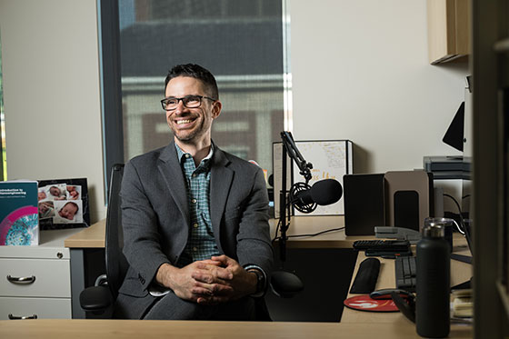 Darren Lipomi, smiling and sitting at his desk surrounded by video and audio recording equipment.