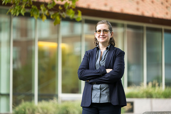 Amanda Stent smiles with their arms crossed in front of Wegmans Hall at the University of Rochester.