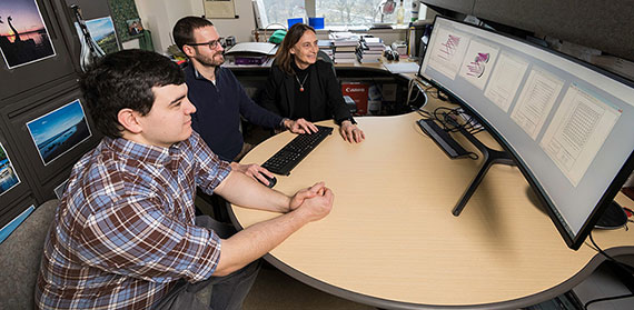 Jannick Rolland sits at a desk with two of her students while reviewing charts and illustrations on a computer screen.