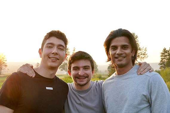 Sidhant Bendre, Michael Giardino, and Achraf Golli embrace in front of a wooded area.