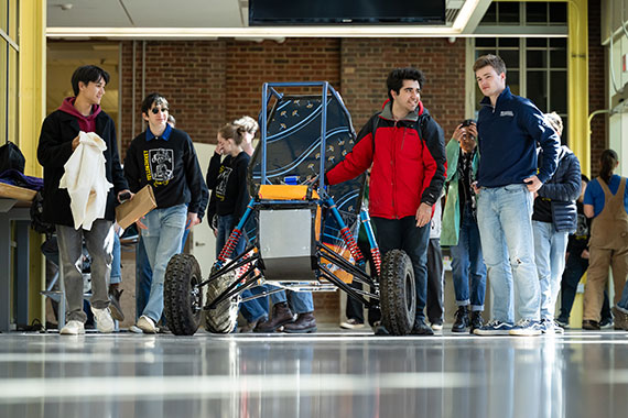 Students stand beside a Baja SAE car in the atrium of Rettner Hall.