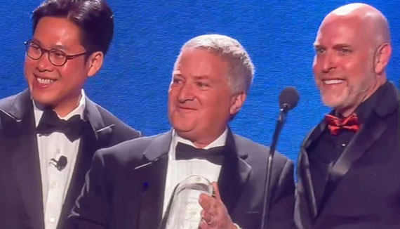 Three men in tuxedos accept a glass award.