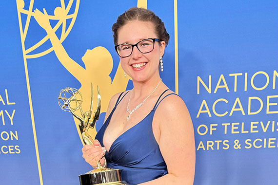 Grace Stensland holds an Emmy Award while at a red carpet event.