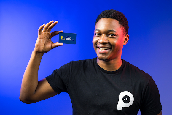 Tamuda Chimhanda holding a PenPal, an NFC-digital business card. He is pictured against a blue background. 