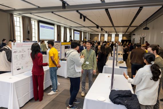 In a crowded room, people view exhibits and talk to presenters during Graduate Research Day 2025.