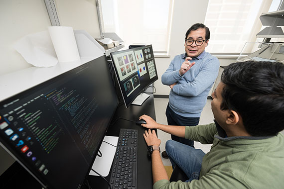 Benjamin Castañeda and Emilio Ochoa converse while reviewing data displayed on multiple computer screens.