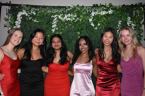 Seven students wearing dresses pose in front of an ivy backdrop at the Engineering Ball.