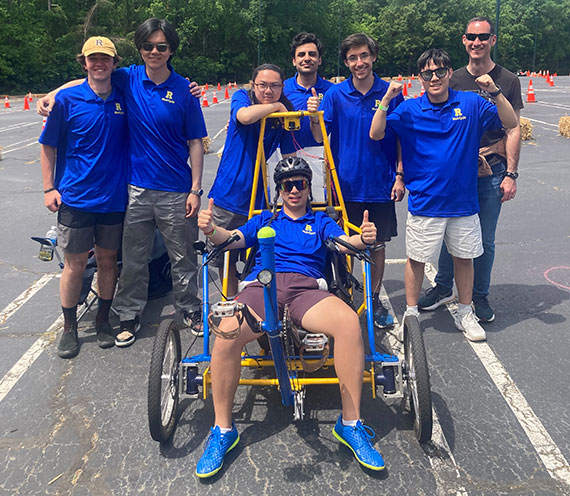Seven students and their faculty advisor pose with a human powered vehicle they designed.