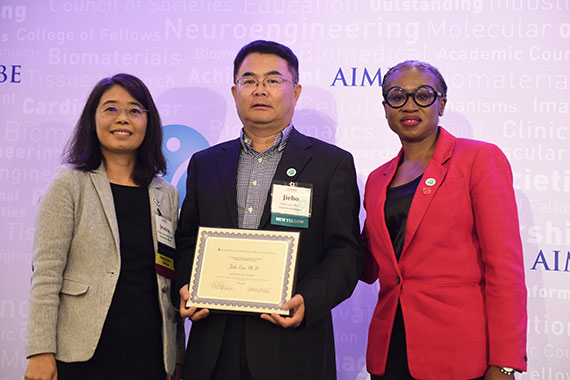 Jiebo Luo, enter stands beside two women while holding a certificate shwoing his induction into the AIMBE College of Fellows.