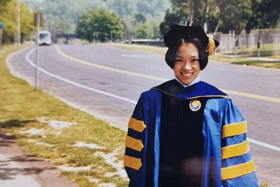 A photograph of Joanne Law standing on Intercampus Drive while wearing her graduation cap and gown regalia when she graduated in 1998.