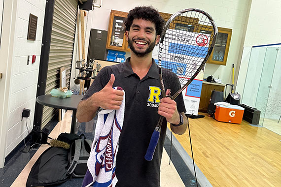 Amar Zakaria gives a thumbs up while holding a racquet at a squash court.