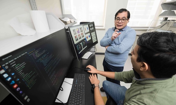 Benjamin Castañeda and Emilio Ochoa converse while reviewing data displayed on multiple computer screens.