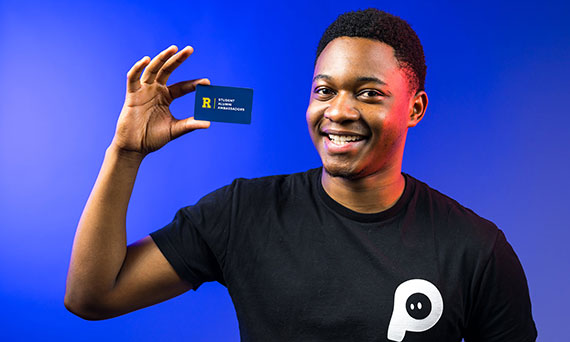 Tamuda Chimhanda holds up a business card with the Rochester Alumni Ambassadors logo on it.