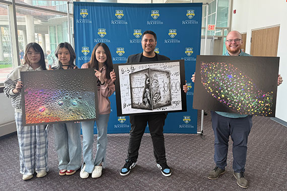 The student winners of the Ed and Barbara Hajim Art of Science competition hold up large prints of their winning artwork in the Carlson Library.
