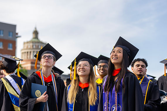 Students in their commencement cap and gown look upward to the sky.