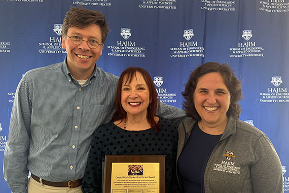 Steve McAleavey, Taimi Marple, and Wendi Heinzelman smile in front of a backdrop with the Hajim School logo.