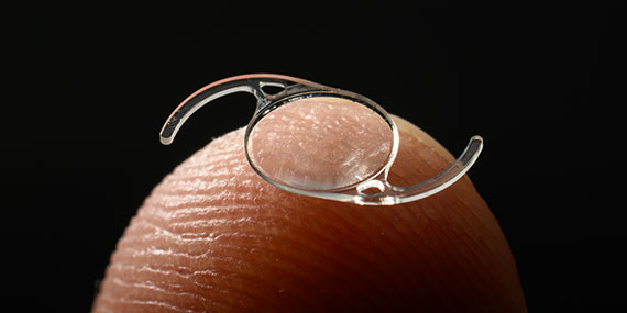 An intraocular lens photographed on a fingertip to show scale.