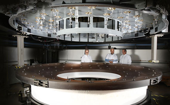 Three scientists in lab coats inspect a mirror 3.5 meters in diameter intended for use at the Vera C. Rubin Observatory.