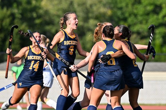 Women's field hockey players celebrate on the field. 