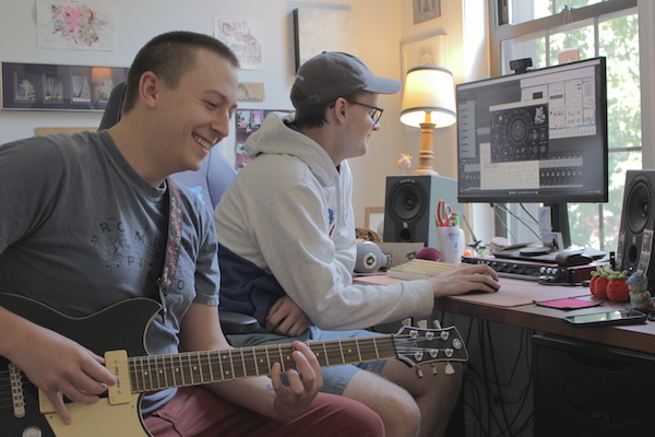 Daniel Fine and Ben Schmitz in a studio. Fine has a guitar and Schmitz is working on a computer. 