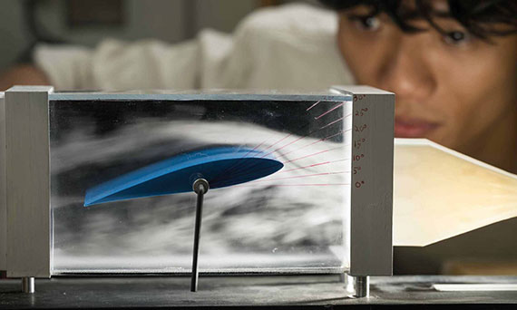 A student examines the wind as it flows around a model of an airplane wing.