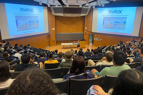 Wendi Heinzelman stands onstage between two large screens while speaking to hundreds of students in the Hubble Auditorium.