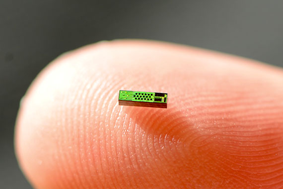 A photonic chip delicately rests on the tip of a finger.