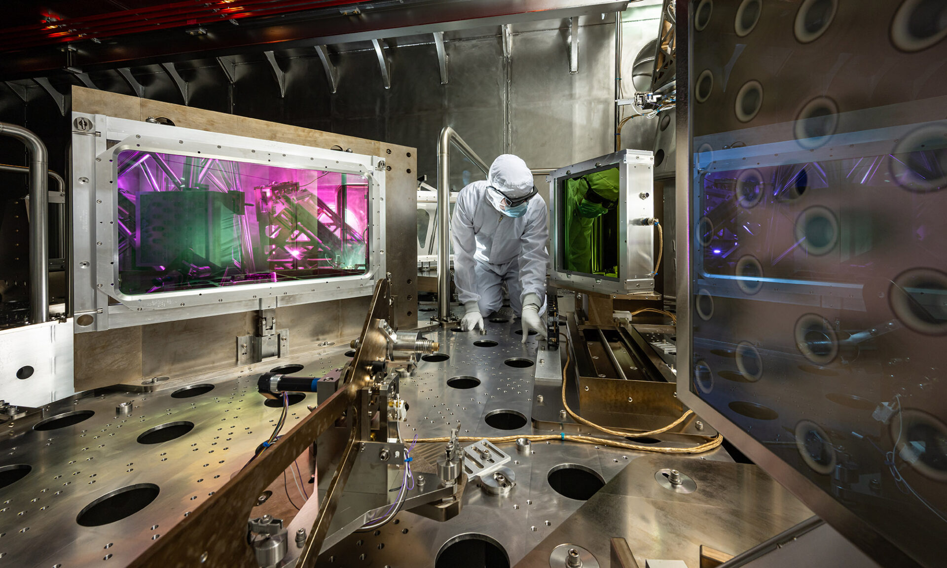 A person in protective gear works inside a high-tech laser research facility with glowing panels and precision equipment.
