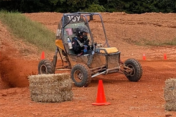 The University of Rochester's Baja SAE car drives on a road course marked by hay bales and traffic cones.