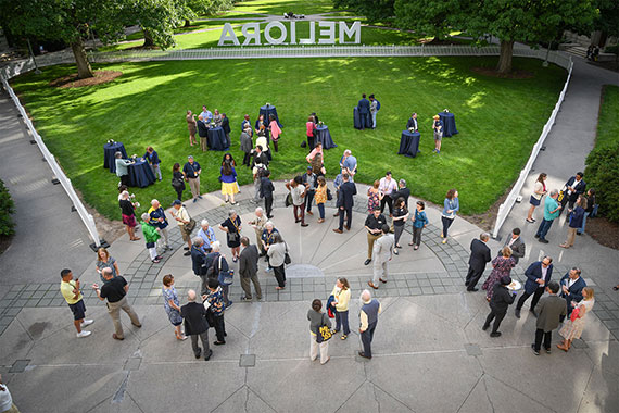 A crowd mingles in front of the steps of the Rush Rhees Library.