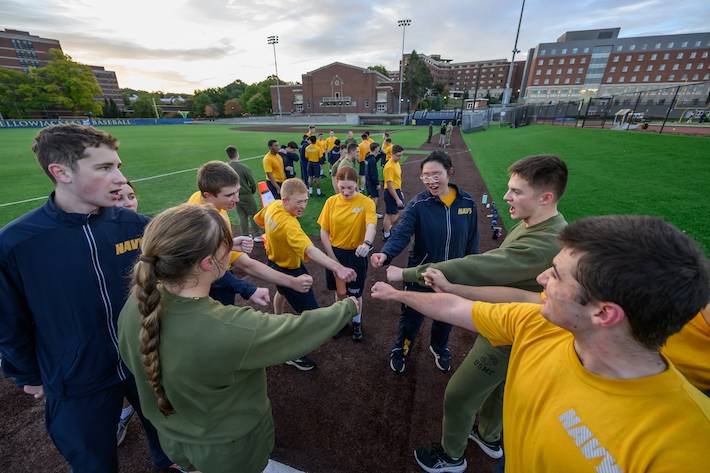 NROTC students put their arms the center of the circle they are standing in.